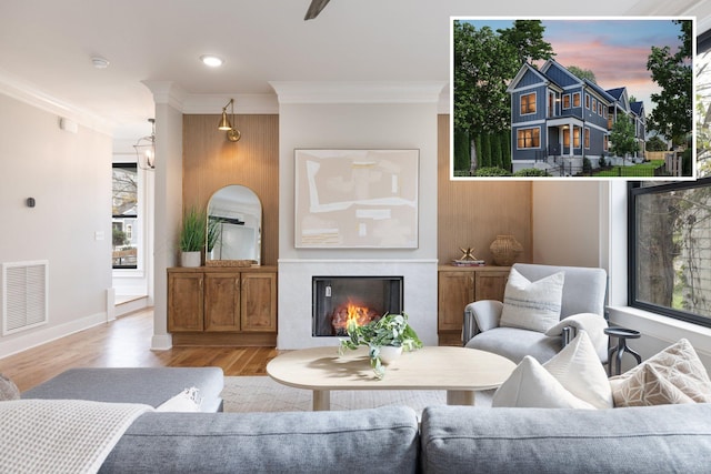 living area with a lit fireplace, wood finished floors, visible vents, and crown molding