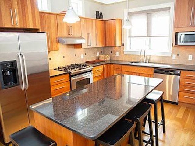 kitchen featuring a kitchen island, a breakfast bar, pendant lighting, dark stone counters, and stainless steel appliances