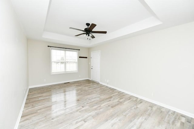 empty room with ceiling fan, baseboards, a raised ceiling, and wood finished floors