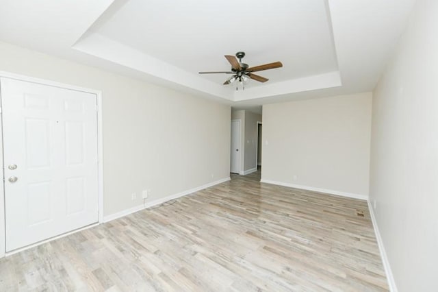 empty room with light wood finished floors, ceiling fan, a raised ceiling, and baseboards