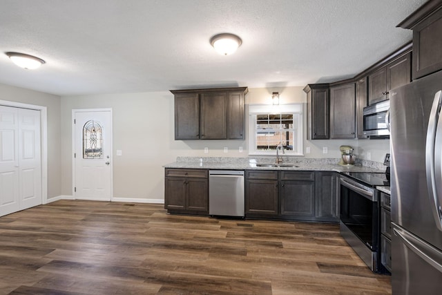 kitchen featuring dark hardwood / wood-style flooring, dark brown cabinetry, light stone countertops, sink, and appliances with stainless steel finishes