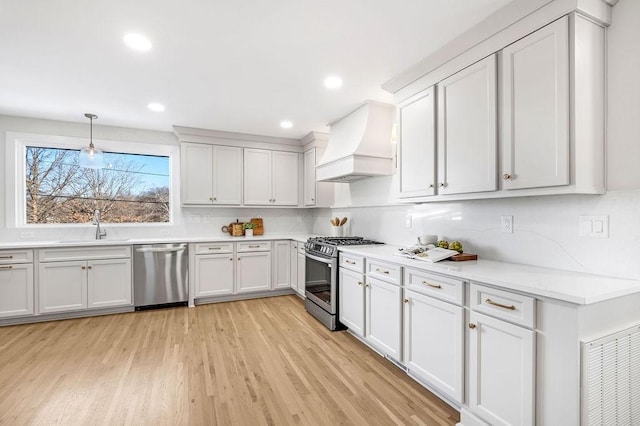 kitchen featuring appliances with stainless steel finishes, sink, white cabinets, hanging light fixtures, and custom range hood