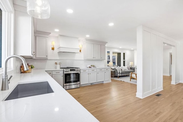 kitchen featuring pendant lighting, white cabinetry, sink, custom exhaust hood, and gas range