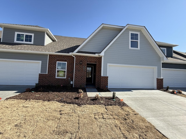 view of front of home with brick siding, a shingled roof, a garage, and concrete driveway