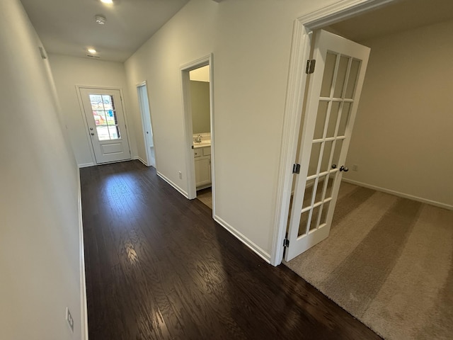 corridor featuring dark wood-type flooring, a sink, and baseboards