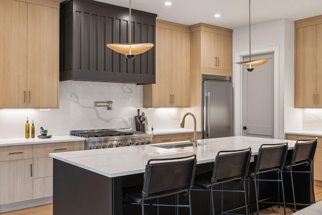 kitchen featuring a kitchen bar, sink, an island with sink, built in fridge, and pendant lighting