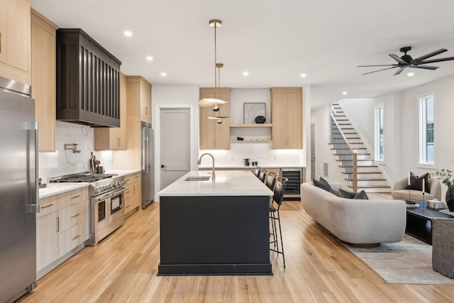 kitchen with pendant lighting, sink, a kitchen island with sink, high quality appliances, and light brown cabinetry