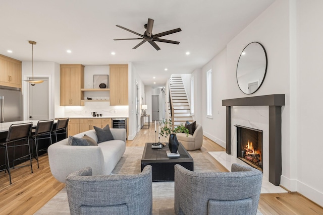 living room featuring a premium fireplace, ceiling fan, wine cooler, and light wood-type flooring