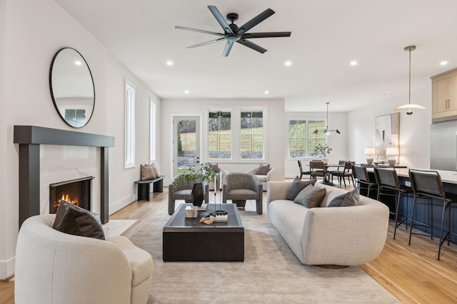 living room with a high end fireplace, light hardwood / wood-style flooring, and ceiling fan