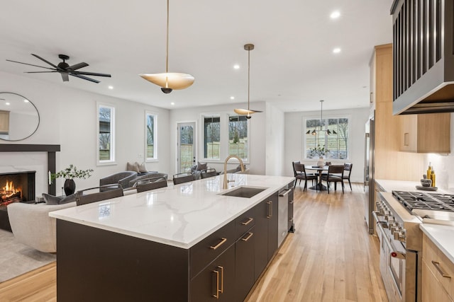 kitchen with decorative light fixtures, high quality appliances, sink, light brown cabinets, and a center island with sink