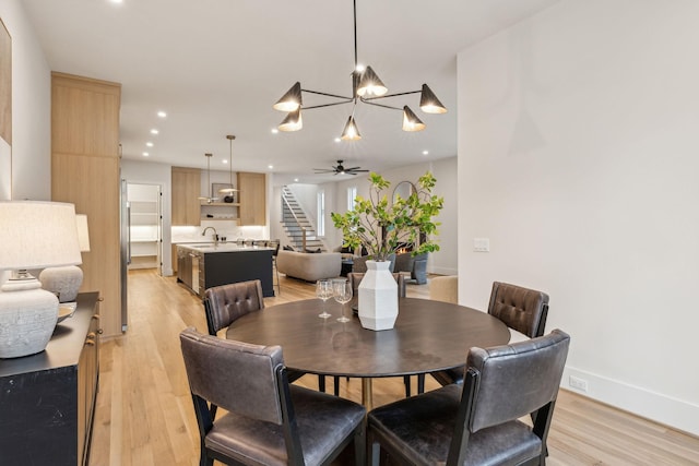 dining room with sink, ceiling fan with notable chandelier, and light hardwood / wood-style flooring