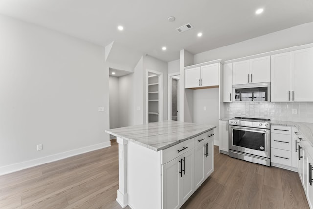 kitchen with white cabinetry, a center island, light stone countertops, stainless steel range oven, and light wood-type flooring