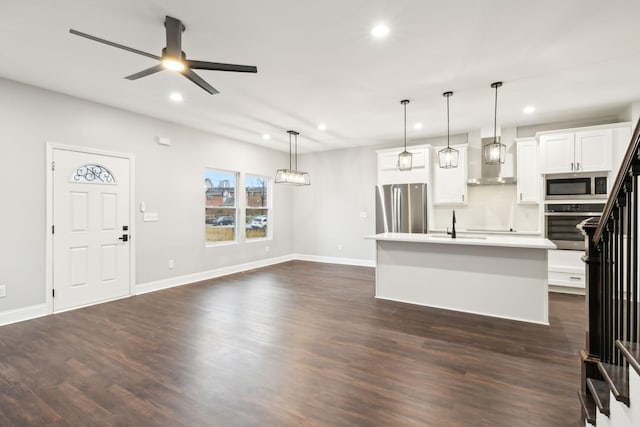 kitchen with dark wood-type flooring, appliances with stainless steel finishes, white cabinets, a center island with sink, and decorative light fixtures