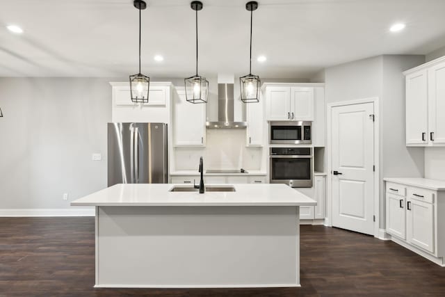 kitchen featuring wall chimney range hood, sink, appliances with stainless steel finishes, hanging light fixtures, and a center island with sink