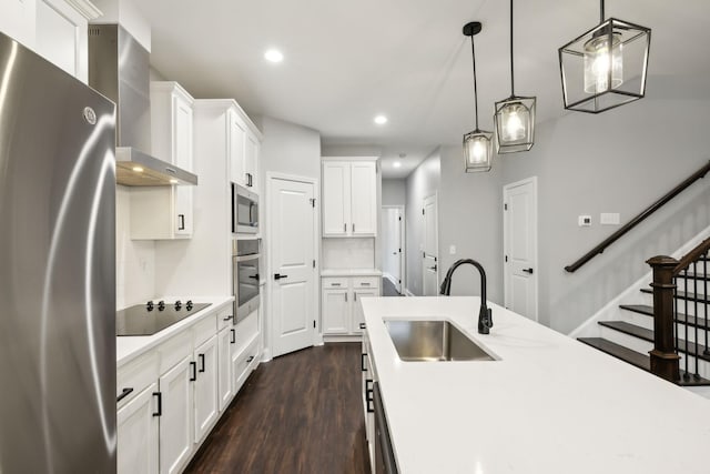 kitchen featuring sink, hanging light fixtures, appliances with stainless steel finishes, white cabinets, and wall chimney range hood