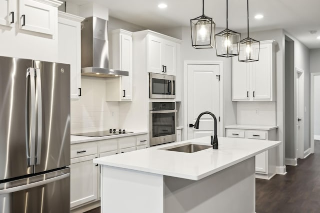 kitchen with sink, hanging light fixtures, appliances with stainless steel finishes, a kitchen island with sink, and wall chimney range hood