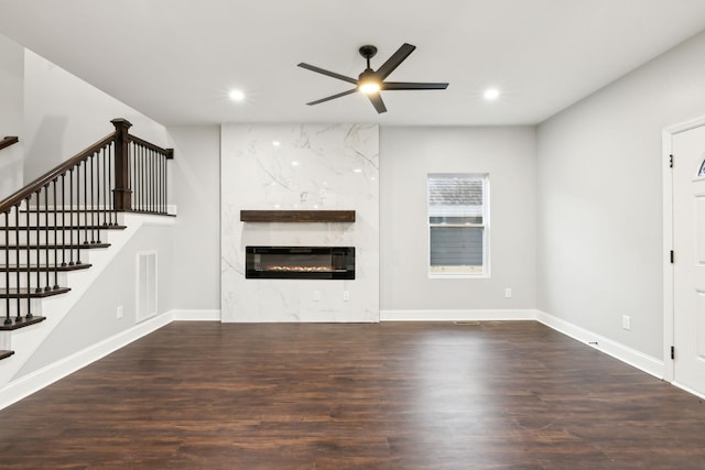 unfurnished living room with a premium fireplace, dark wood-type flooring, and ceiling fan