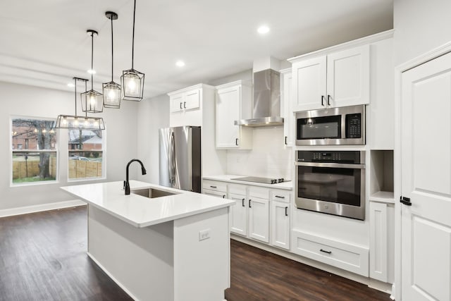 kitchen featuring wall chimney exhaust hood, sink, white cabinetry, appliances with stainless steel finishes, and a kitchen island with sink