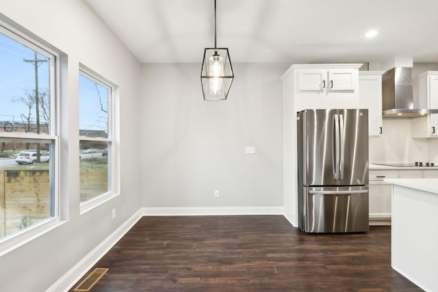 kitchen with wall chimney range hood, stainless steel fridge, hanging light fixtures, white cabinets, and dark hardwood / wood-style flooring