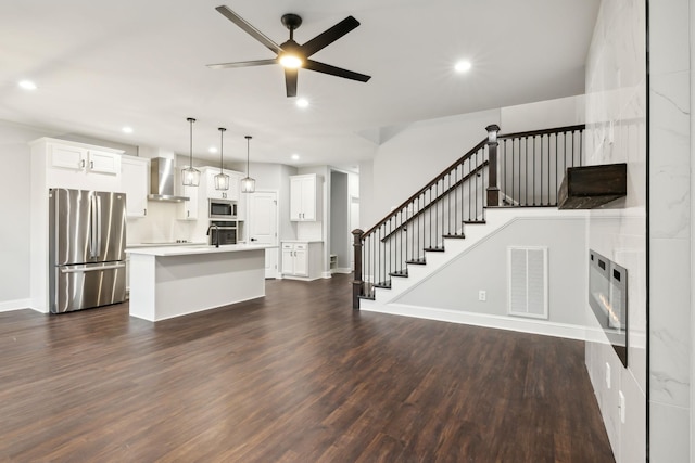 kitchen with appliances with stainless steel finishes, white cabinetry, a kitchen island, decorative light fixtures, and wall chimney exhaust hood