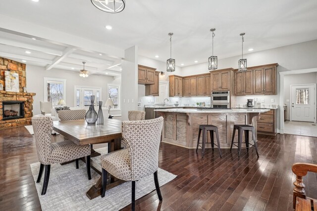 dining area featuring a stone fireplace, beamed ceiling, sink, coffered ceiling, and dark wood-type flooring