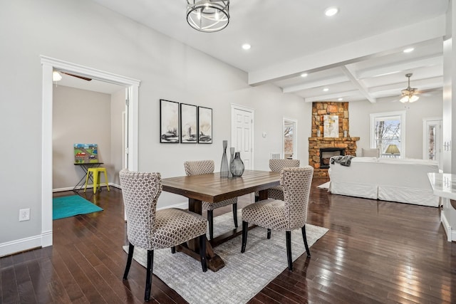 dining area with ceiling fan, a stone fireplace, dark hardwood / wood-style floors, and beam ceiling