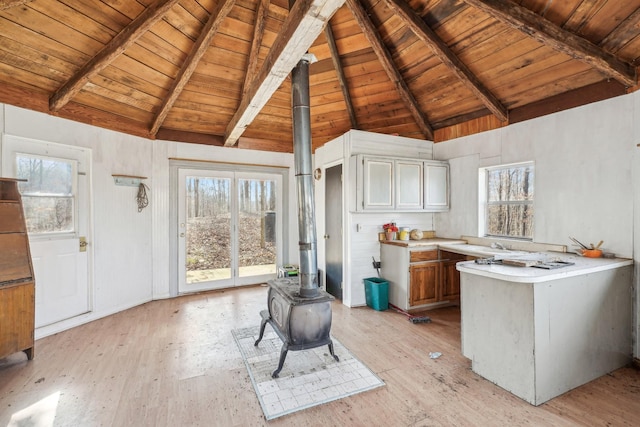 kitchen with vaulted ceiling with beams, wood ceiling, light hardwood / wood-style flooring, and a wood stove