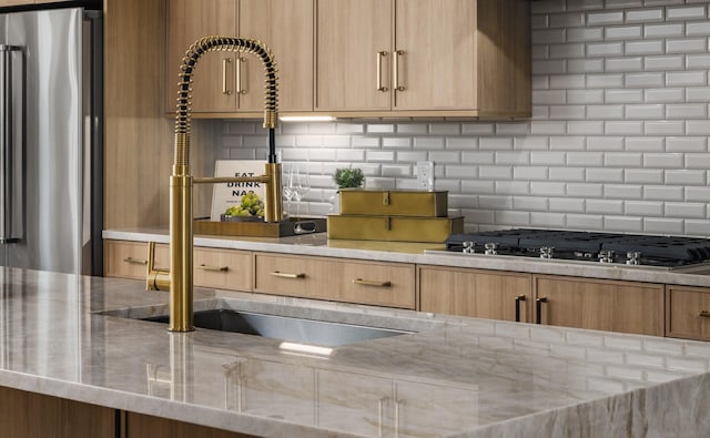 kitchen with stainless steel appliances, light stone countertops, sink, and backsplash