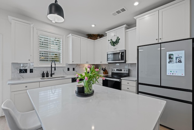 kitchen featuring pendant lighting, tasteful backsplash, sink, white cabinets, and stainless steel appliances