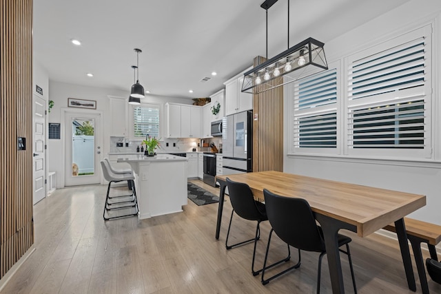 kitchen featuring a kitchen island, white cabinetry, hanging light fixtures, stainless steel appliances, and light hardwood / wood-style flooring