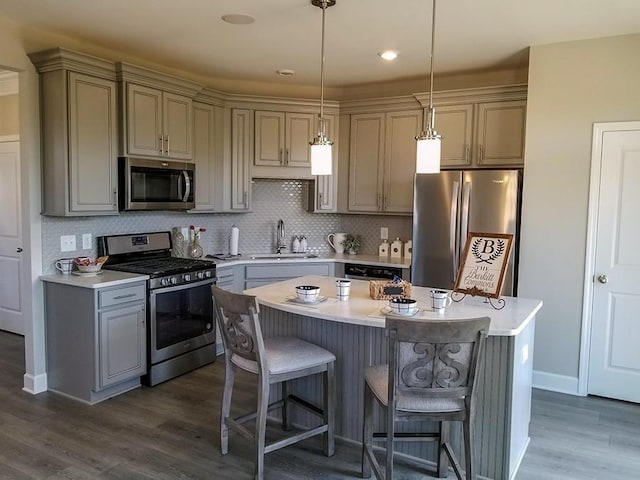 kitchen featuring sink, a kitchen island, pendant lighting, stainless steel appliances, and backsplash