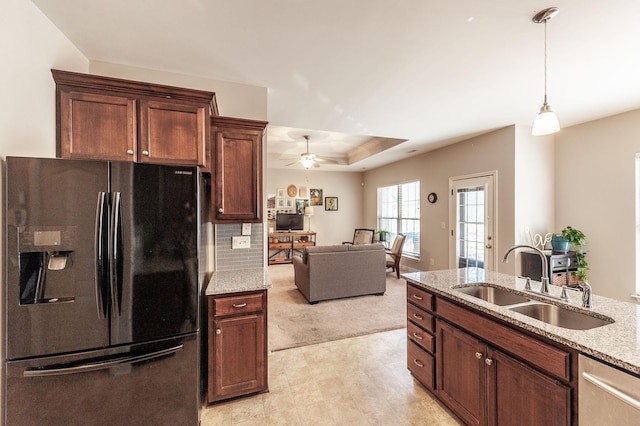 kitchen featuring refrigerator with ice dispenser, sink, pendant lighting, a raised ceiling, and light stone countertops