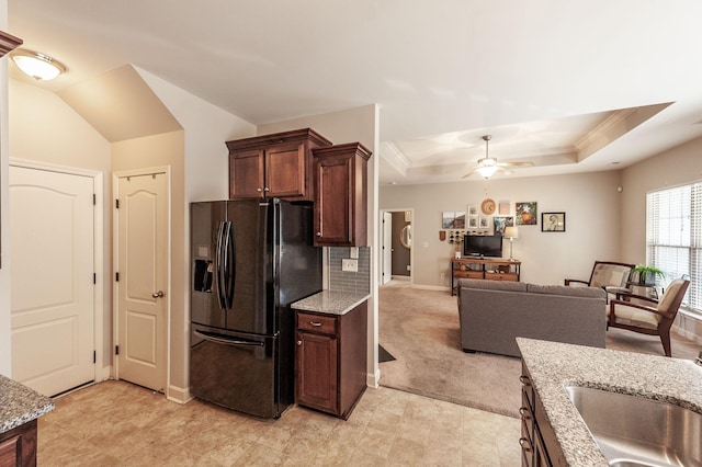 kitchen featuring tasteful backsplash, light stone countertops, ceiling fan, a tray ceiling, and black fridge