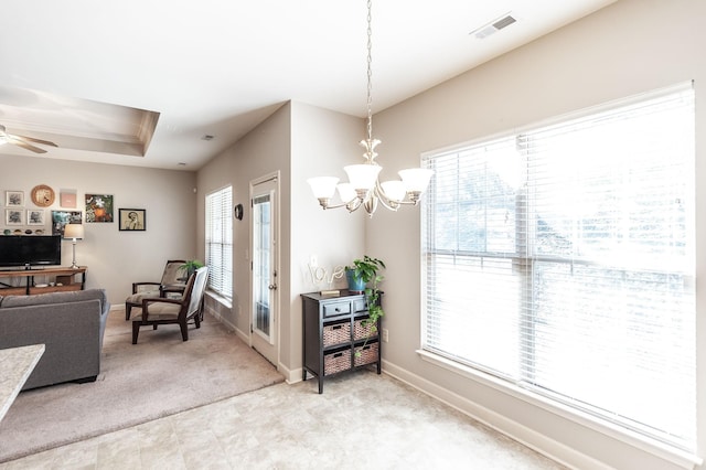 interior space with ceiling fan with notable chandelier, plenty of natural light, a raised ceiling, and light carpet