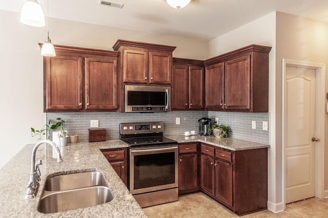 kitchen with appliances with stainless steel finishes, light stone counters, decorative backsplash, decorative light fixtures, and sink