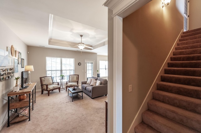 living room with a raised ceiling, ceiling fan, and light colored carpet