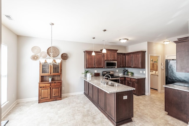 kitchen featuring washer and dryer, stainless steel appliances, pendant lighting, sink, and kitchen peninsula