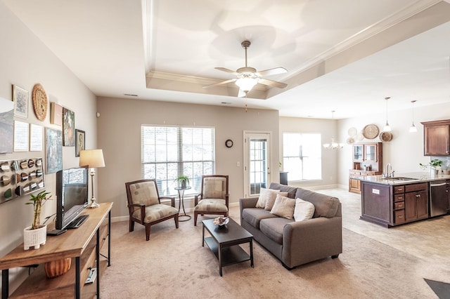 carpeted living room featuring ceiling fan with notable chandelier, a tray ceiling, ornamental molding, and sink