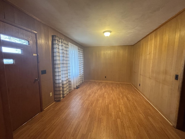 entrance foyer with crown molding, wooden walls, and light hardwood / wood-style floors