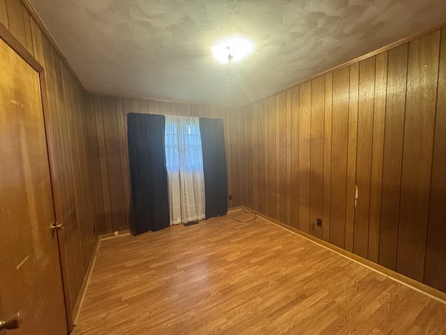 empty room with light hardwood / wood-style flooring and wooden walls