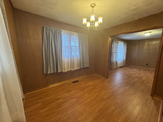 empty room featuring wooden walls, a chandelier, and hardwood / wood-style floors