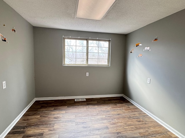 spare room featuring dark wood-type flooring and a textured ceiling