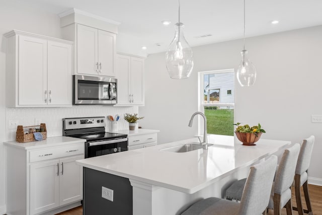 kitchen featuring pendant lighting, white cabinetry, sink, stainless steel appliances, and a center island with sink