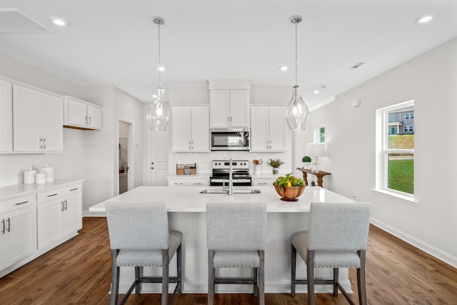 kitchen with pendant lighting, an island with sink, white cabinetry, decorative backsplash, and stainless steel appliances