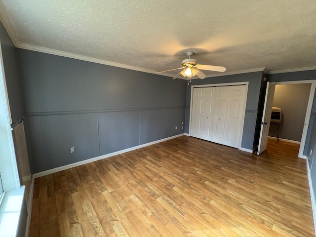 unfurnished bedroom featuring a closet, a textured ceiling, wood finished floors, and wainscoting