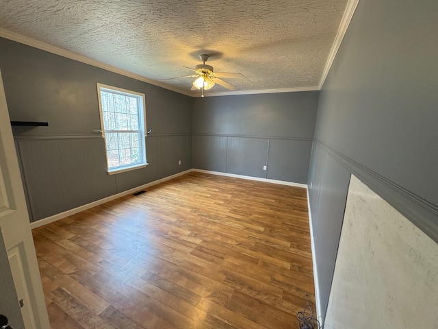 unfurnished room featuring a wainscoted wall, ornamental molding, a textured ceiling, and wood finished floors