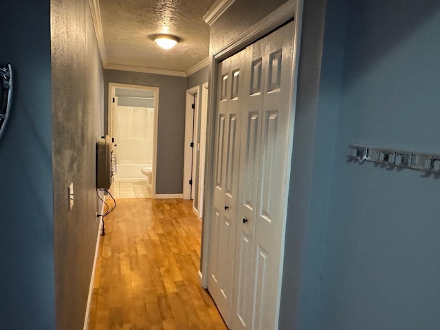 corridor with a textured ceiling, crown molding, and light wood finished floors