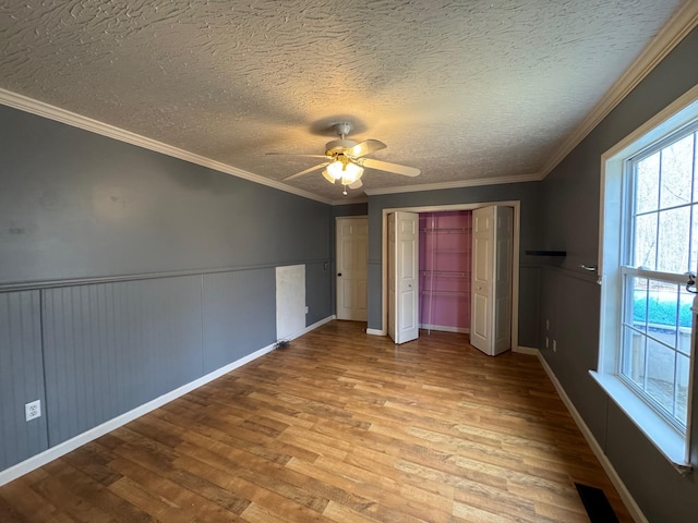 unfurnished bedroom with a wainscoted wall, ornamental molding, wood finished floors, a textured ceiling, and a ceiling fan