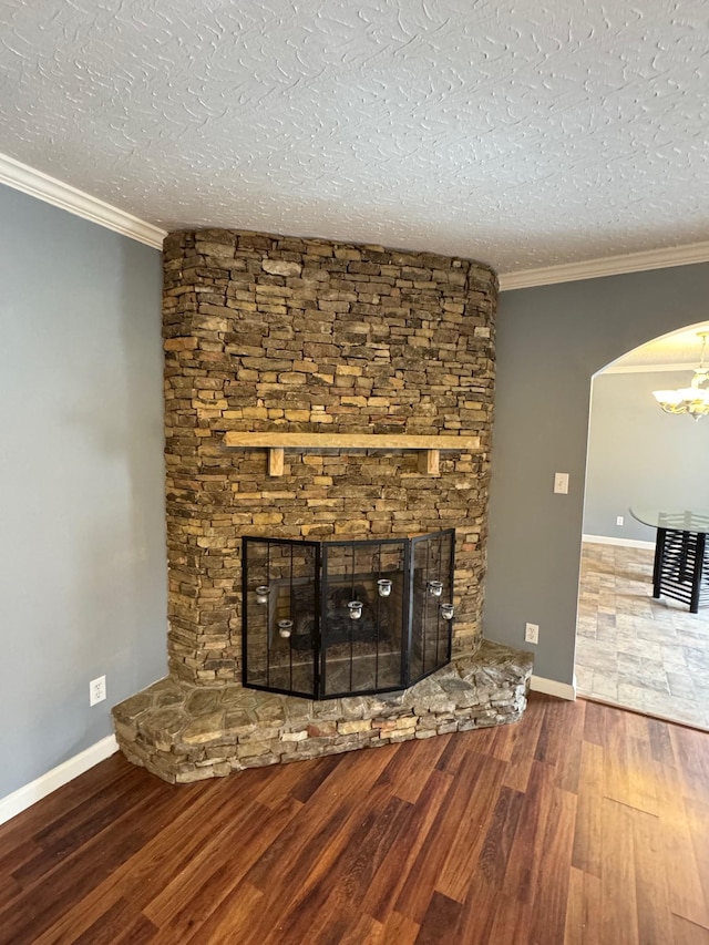 unfurnished living room with a stone fireplace, a textured ceiling, crown molding, and wood finished floors