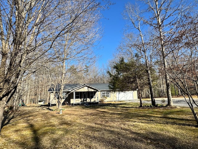 view of front facade with metal roof, driveway, covered porch, and a front yard